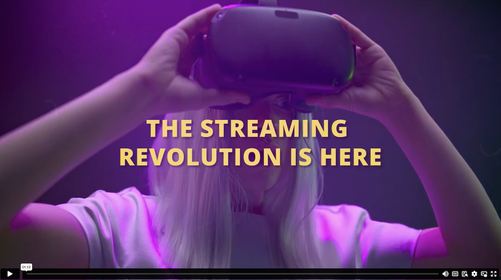 Still image for the Business of Entertainment sizzle reel video. Image shows a blonde woman holding a VR headset up to her face. Screen capture has yellow text that reads, 'The Streaming Revolution is Here.'